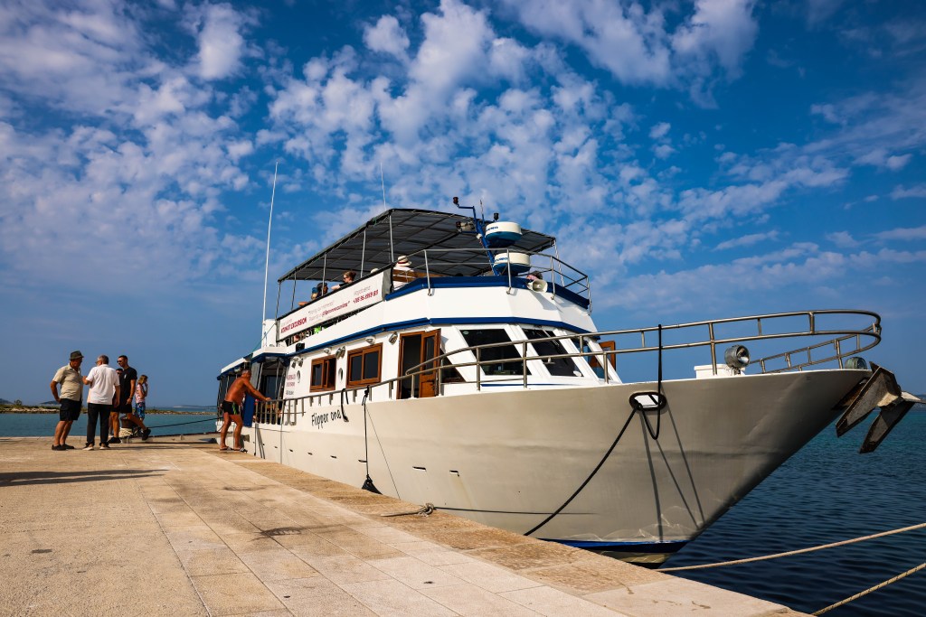 Flipper One excursion boat docked at Pakoštane harbor, ready to board passengers for Kornati and Telašćica tour under a bright blue sky.