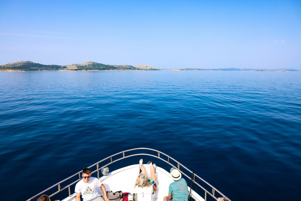 View from the bow of a boat heading from Pakoštane toward Kornati National Park — passengers enjoying the calm Adriatic Sea during a guided island tour.