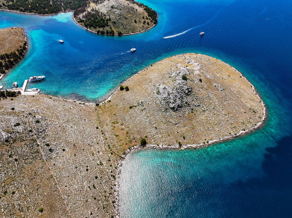 Aerial view of Katina Island in Kornati National Park — turquoise Adriatic waters, peaceful cove, and boat docked at a quiet pier, perfect for swimming and solo island exploration.