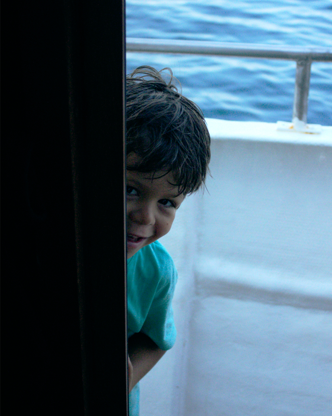 Little boy playfully peeking through the boat cabin doorway during a sea adventure.